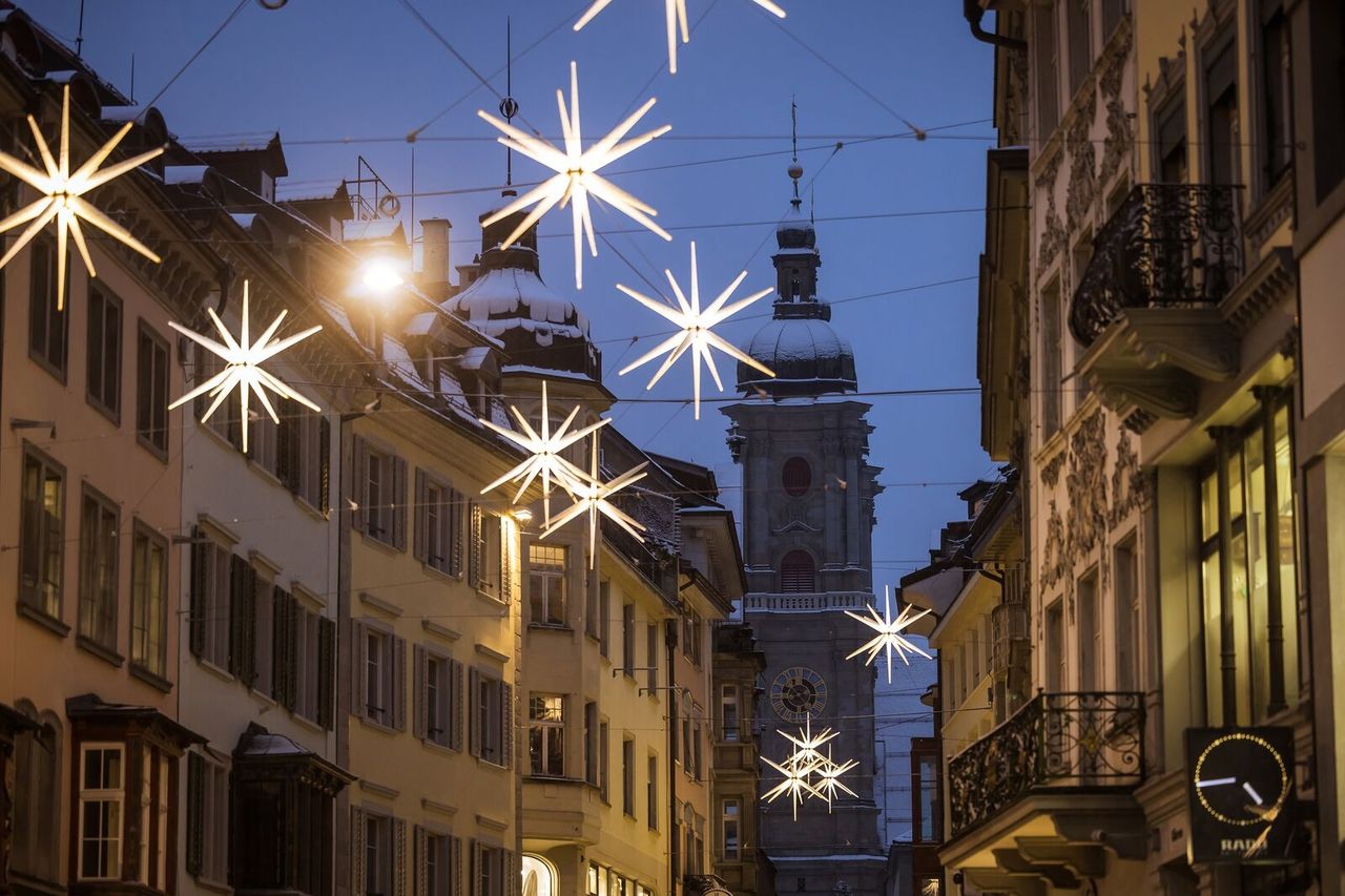 Glowing stars above an old-town lane at dusk, a tower of the cathedral in the background