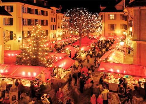 Stalls with red roofs and illuminated trees on Friedhofplatz in the evening, many visitors